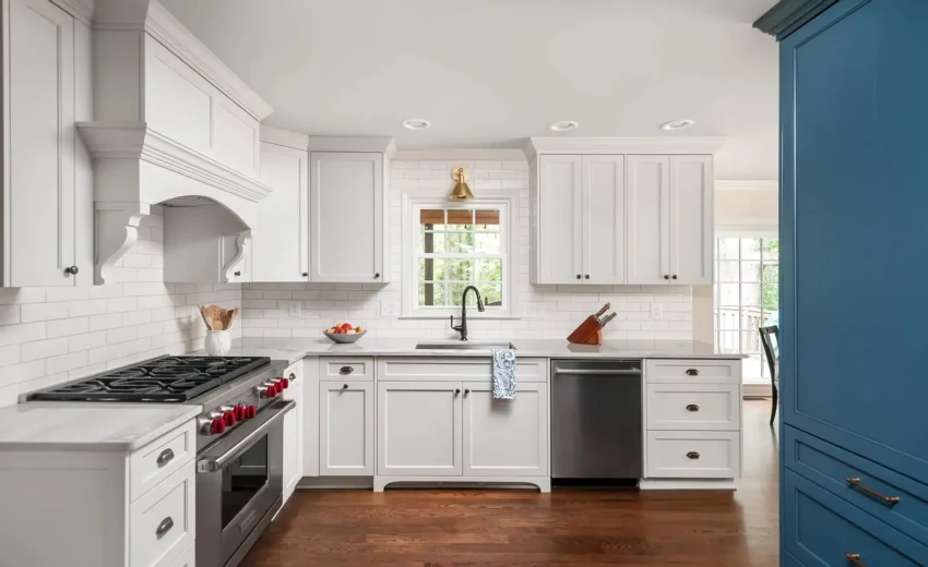 Bright white kitchen with shaker cabinets, blue island, and pendant lighting.