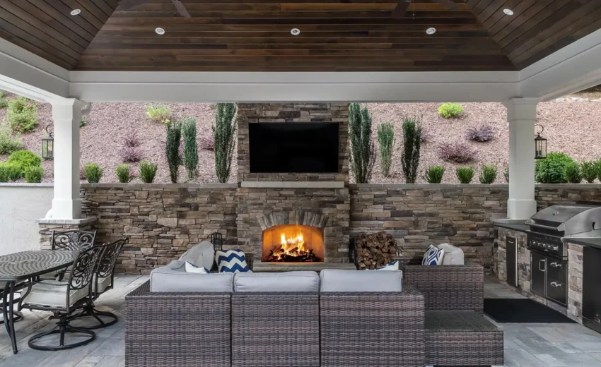 Covered outdoor lounge with stone fireplace, wood ceiling, and modern seating.