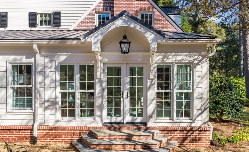Elegant white sunroom addition with brick foundation, arched windows, and black metal lantern light.