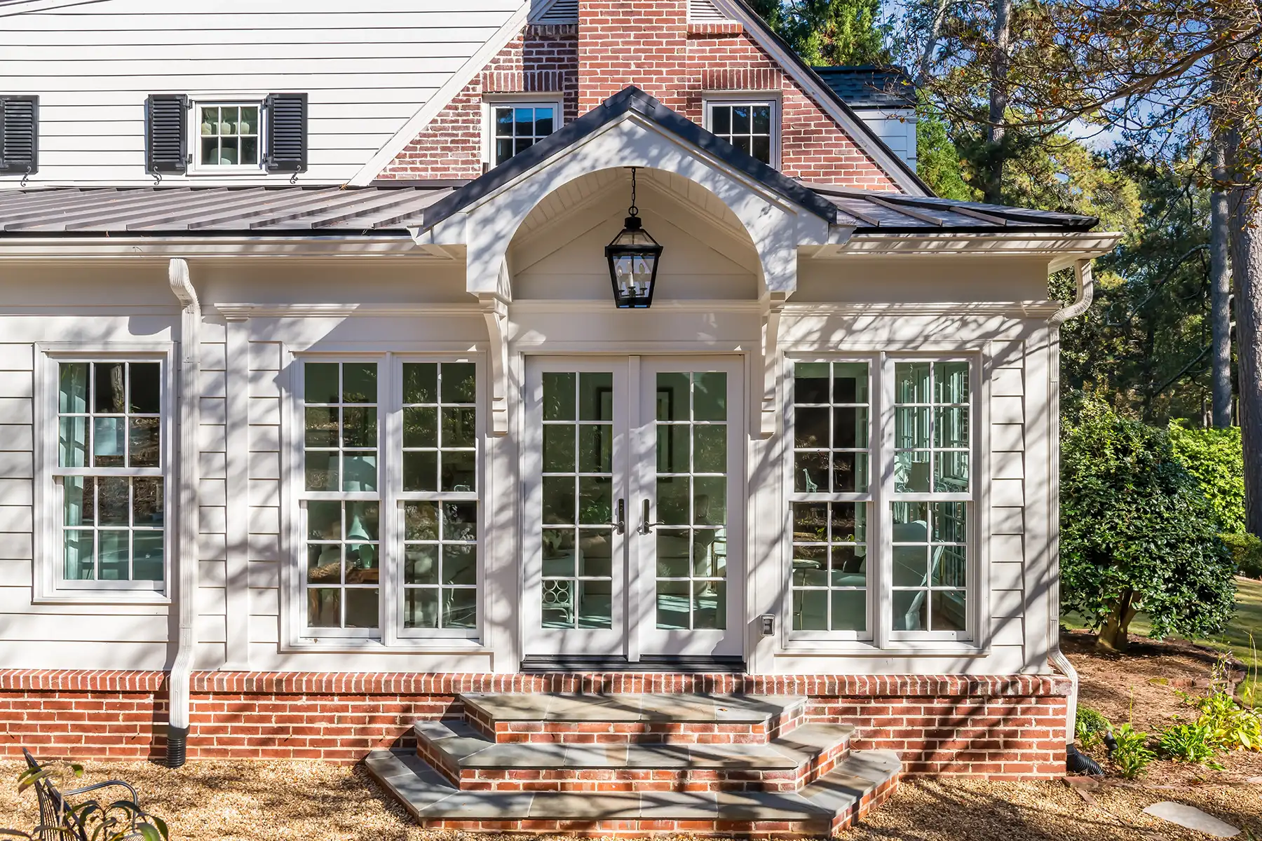 Woodside Rd, Yardley, PA 19067 1 | The Home X Elegant white sunroom addition with brick foundation, arched windows, and black metal lantern light.