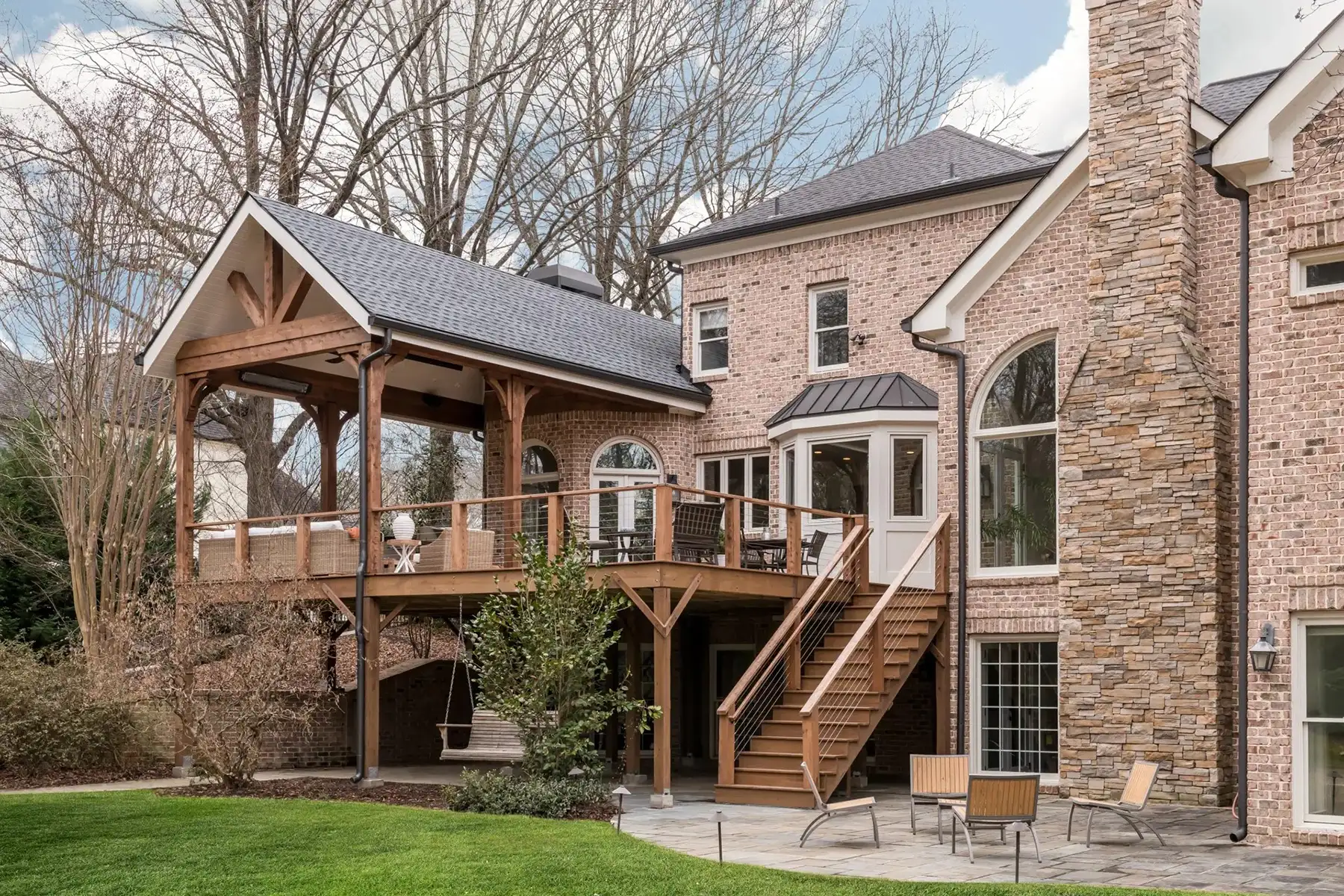 Aquetong Rd, New Hope, Pa 18938 2 | The Home X Rear view of a luxury stone home featuring a covered deck, turret-style bay window, and lush wooded surroundings.