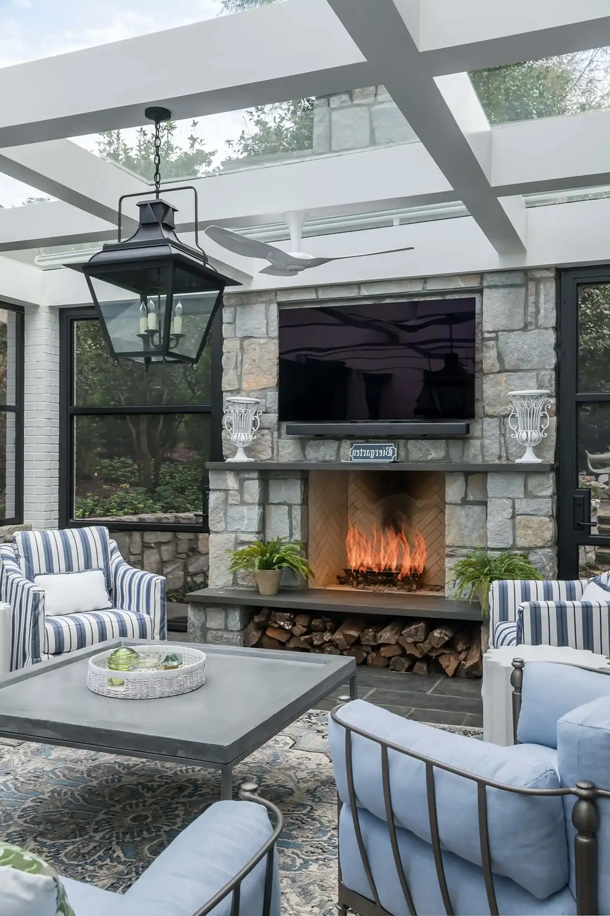Pidcock Creek Rd, New Hope, PA 18938 2 | The Home X Stone fireplace with mounted TV in luxury sunroom with outdoor seating and glass ceiling in New Hope, PA.