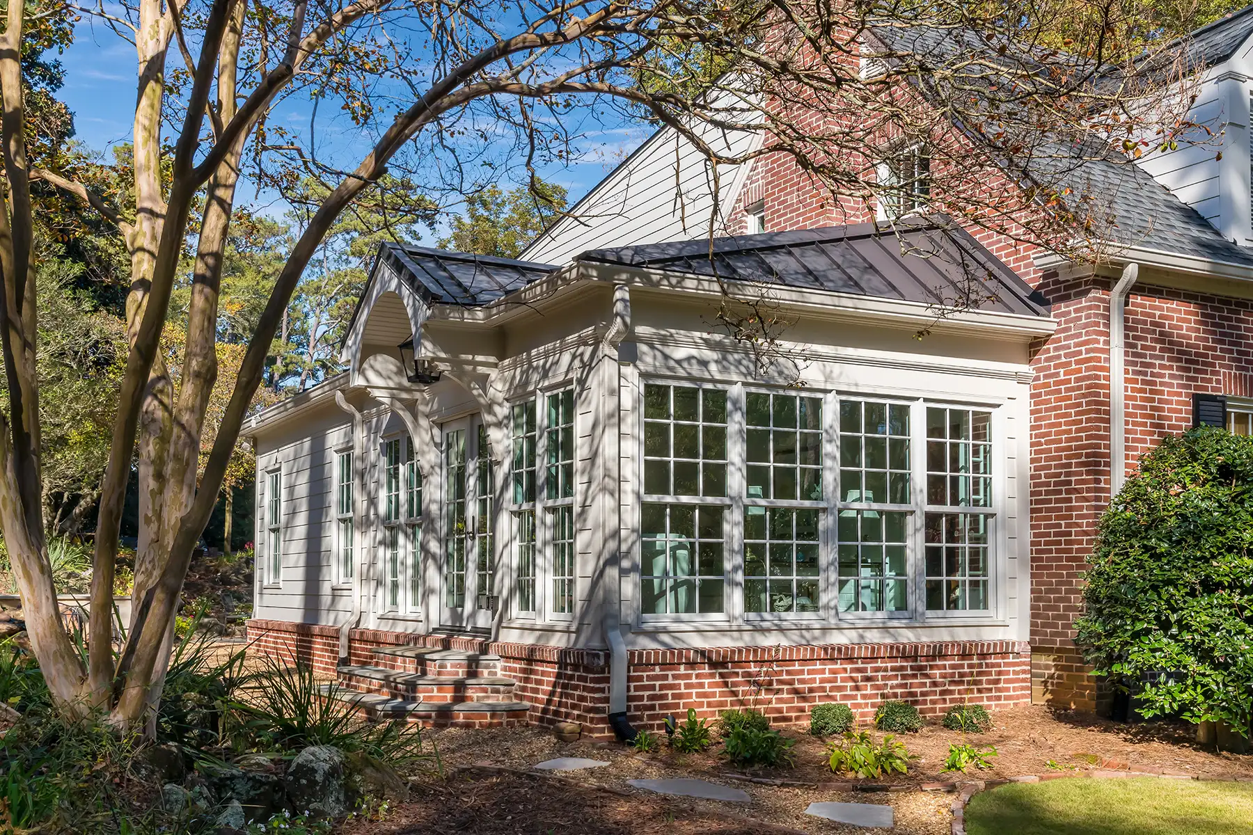 Woodside Rd, Yardley, PA 19067 2 | The Home X Backyard view of classic white sunroom addition with French doors, brick skirt, and mature landscaping.