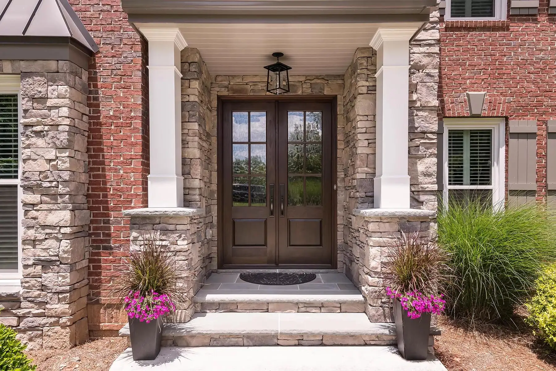 Sugan Rd, New Hope, PA 18938 3 | The Home X Covered front entry with stone columns, double glass doors, and potted flowers on a brick and stone home.