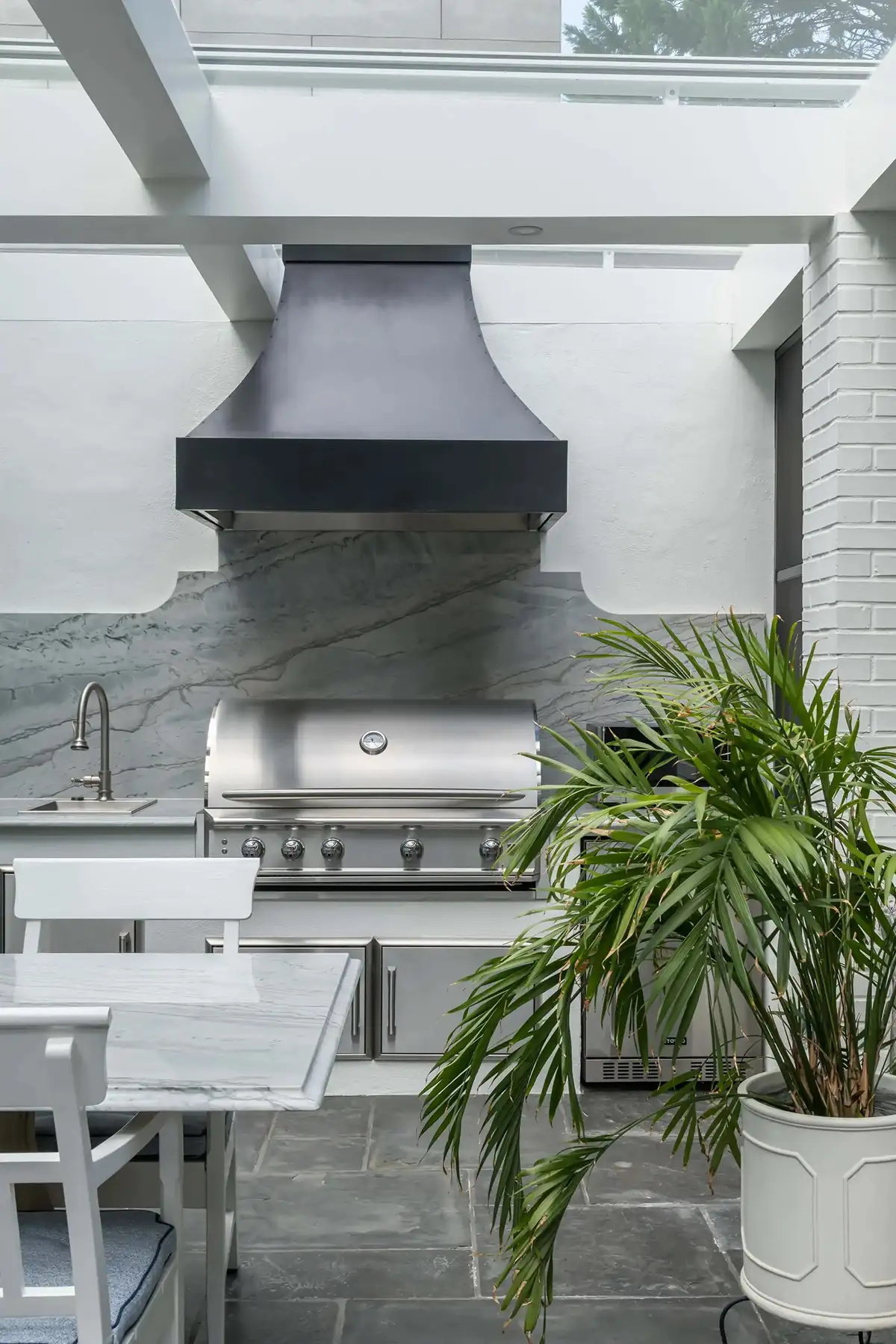 Pidcock Creek Rd, New Hope, PA 18938 4 | The Home X Contemporary outdoor kitchen with a bold black range hood, grill, and seating in a glass-covered patio in New Hope, PA.