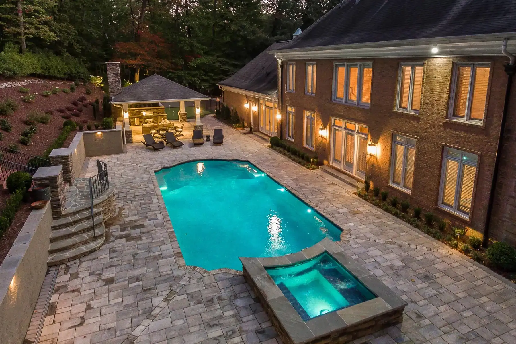 Sergeantsville Rd, Delaware Twp., 08559 10 | The Home X Evening view of a luxurious illuminated pool and spa surrounded by pavers, adjacent to an elegant brick home.
