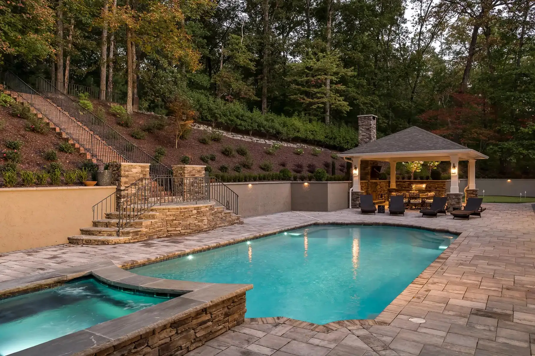 Sergeantsville Rd, Delaware Twp., 08559 12 | The Home X Luxurious outdoor pool area with raised spa, stone decking, and a pool house surrounded by trees.