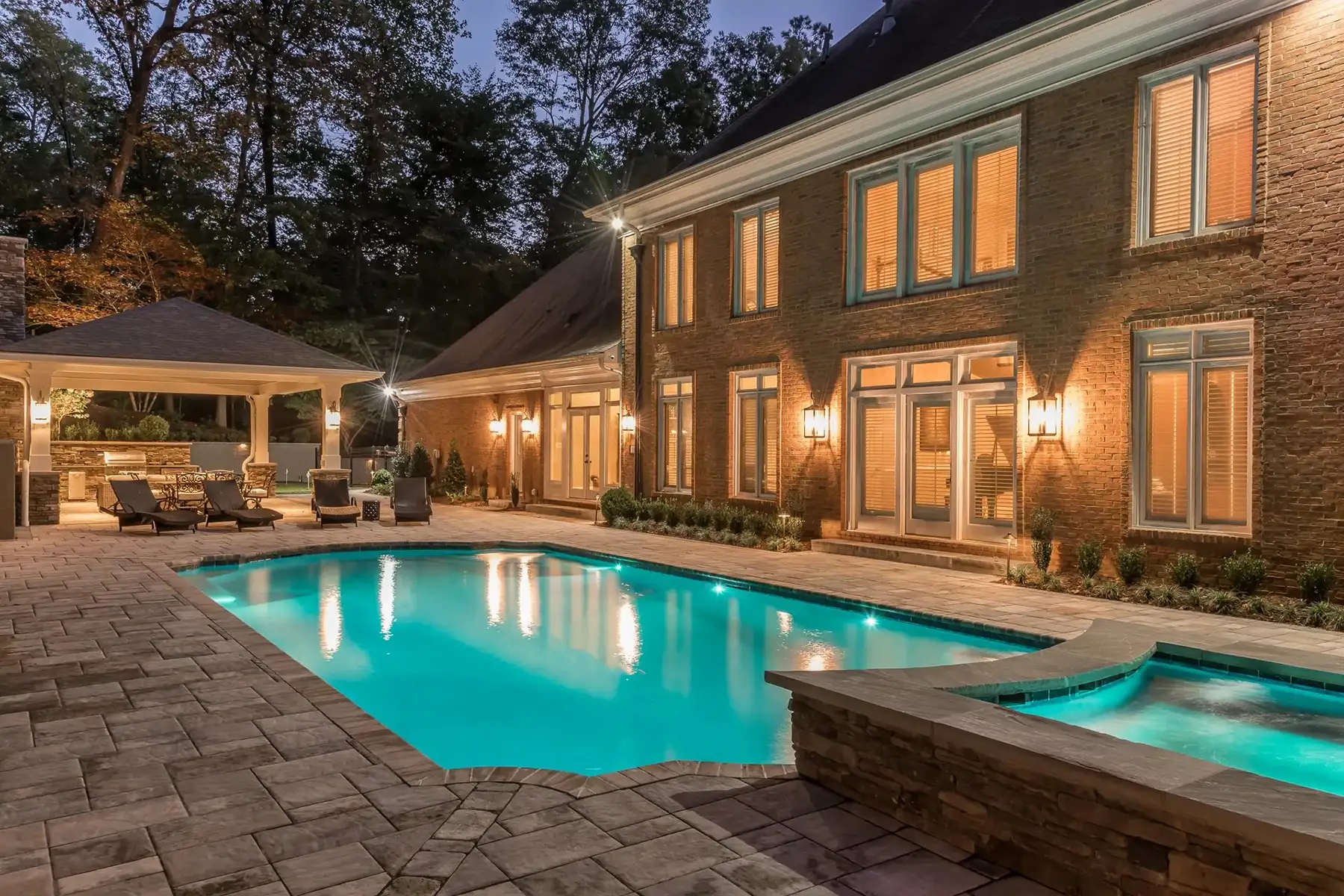 Sergeantsville Rd, Delaware Twp., 08559 13 | The Home X Evening view of a luxury pool with spa, illuminated stone patio, and elegant home exterior in Delaware Township.