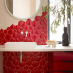 Custom red upholstered wall panel with modern sconces and curved mirror feature by The Home X.