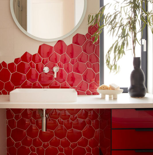 Custom red upholstered wall panel with modern sconces and curved mirror feature by The Home X.