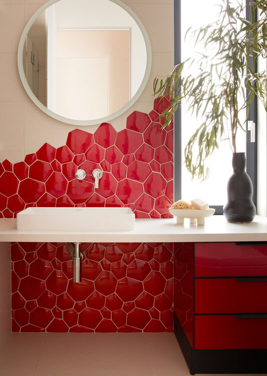 Custom red upholstered wall panel with modern sconces and curved mirror feature by The Home X.