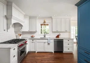 Bright white kitchen with shaker cabinets, blue island, and pendant lighting.