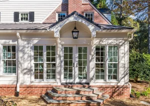 Elegant white sunroom addition with brick foundation, arched windows, and black metal lantern light.