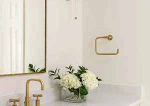 Bright bathroom vanity with gold wall-mounted faucet, vertical sconce lighting, and a white quartz countertop.
