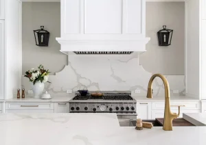 Elegant kitchen island with brass gooseneck faucet, white quartz counters, and sleek black sconces.