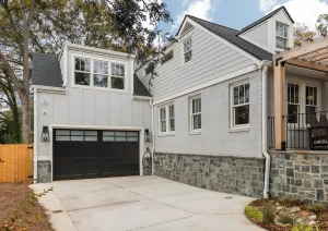 Modern white home exterior with black garage door, natural wood fencing, and finished driveway.