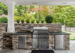 Outdoor kitchen with built-in stainless grill, stone bar, and spacious countertop beneath covered pavilion.