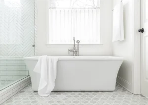 Freestanding bathtub with wall-mounted faucet and classic wainscoting in a bright white bathroom.