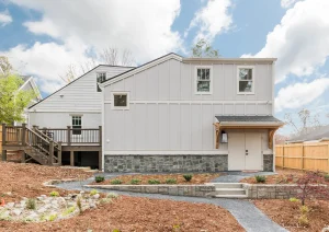 Back view of modern white home with raised deck, black-framed windows, and natural landscaping.