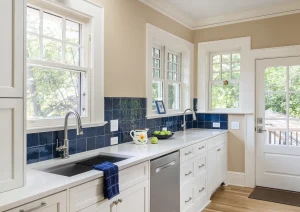 Bright kitchen corner with white cabinets, navy backsplash, and wraparound windows offering natural light.