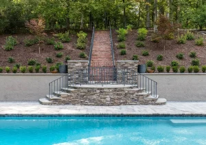 Stone staircase descending to a poolside waterfall with tiered landscaping.