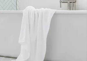 Freestanding soaking tub with wall-mounted faucet and white towel draped over the edge.