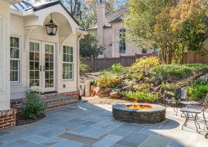 Backyard view of elegant sunroom addition with tiered landscaping, stone retaining walls, and curved paver patio.