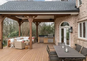 Outdoor entertaining space with composite deck, built-in grilling station, stone columns, and wood pergola attached to a brick exterior home.