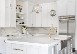 Bright white kitchen with large quartz island, brass sconces, and floating shelves.