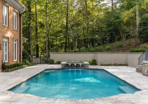 Contemporary in-ground pool with expansive concrete patio and lush woodland views in Delaware Township, NJ.