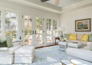 Sunroom with glass French doors, yellow accent pillows, and a view into a lush garden.