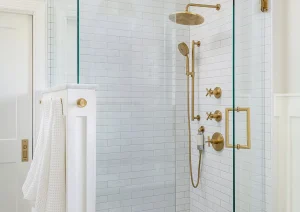 Modern walk-in shower with glass enclosure, brass fixtures, and built-in niche.