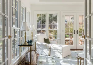 Sunroom with wall-to-wall windows, white furniture, and a round table centered in natural light.