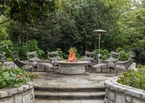 Custom circular stone fire pit with surrounding seating and lush garden landscaping by The Home X in Bucks County.