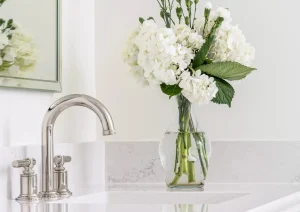 Detail of bathroom sink with gooseneck faucet, white quartz counter, and fresh floral arrangement.