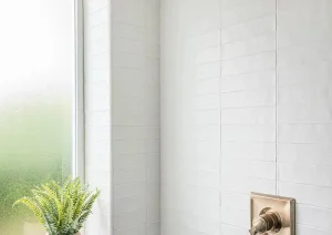 Minimalist shower with vertical white tile, brass fixtures, and a frosted window.