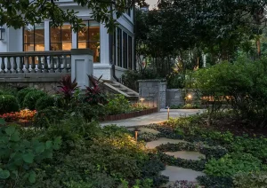Evening garden with a winding stone path, soft landscape lighting, and cottage-style home in the background.