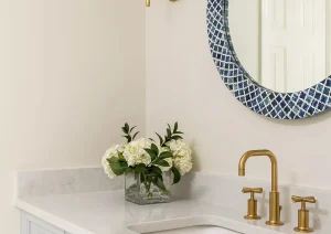 Single bathroom vanity with gold sconce lighting, navy blue textured mirror, and white cabinetry.