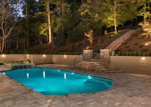 Night view of a glowing swimming pool surrounded by trees with soft landscape lighting in Delaware Township.