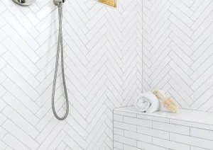Shower corner with white hex tile walls, brass fixtures, and marble mosaic flooring.