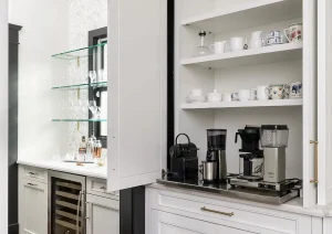 Custom white beverage center with glass shelving, quartz countertop, and built-in wine fridge.
