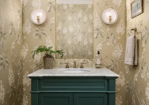 Powder room with botanical wallpaper, dark green vanity, and brass accents.