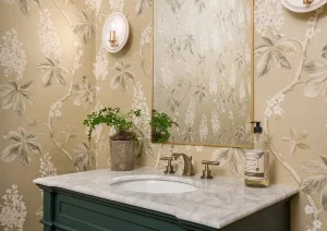 Front-facing view of a moody powder room with floral wallpaper, deep green vanity, and brushed brass faucet.