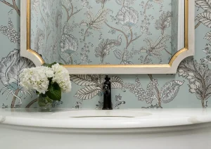 Close-up of a curved white vanity set against botanical wallpaper with brass-framed mirror in a boutique-style bathroom remodel in New Hope, PA.