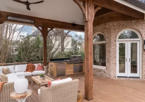 Outdoor living area featuring brick walls, French doors with arched transoms, and exposed wood beams over a natural wood deck.